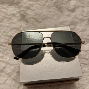 Aviator solglasögon från Gina Tricot - Snygga aviator solglasögon från Gina Tricot med tunna guldfärgade metallbågar och mörka svarta glas. Klassisk och stilren design som ger en cool vibe till din look. Perfekta för soliga dagar och passar till de flesta outfits.