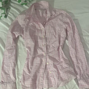 figursydd rosa skjorta från Banana Republic - Snygg rosa skjorta från Banana Republic med rutigt mönster och klassisk krage. Skjortan är figursydd och har långa ärmar samt knappar framtill. Tillverkad i stretchigt bomullsmaterial som är non-iron för extra smidighet.