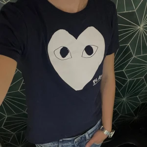 Mörkblå Comme des Garçons Play t-shirt - T-shirt från Comme des Garçons Play med stort vitt hjärta och ögon på bröstet. Klassisk crewneck och korta ärmar. Tryckt PLAY-logga på framsidan. Skön passform.