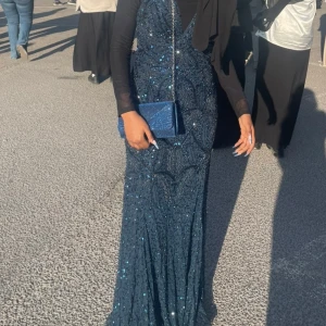 Asos maxi dress  - Säljer en marinblå långklänning med djup v-ringning och glittriga paljettdetaljer i ett elegant mönster. Har använt den en gång innan på min bal. Klänningen har figurnära passform och är täckt av skimrande pärlor och paljetter som ger en lyxig känsla. Perfekt för bal eller festkvällar!