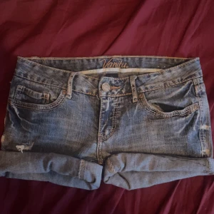 Lågmidjadr Blå jeansshorts från Vanity  - Säljer ett par lågmidjade blå jeansshorts från Vanity med klassisk femficksdesign och uppvikta ben. Shortsen har snygga slitningar och är gjorda i stretchig bomull med lite spandex för extra komfort. Perfekt för dig som gillar en avslappnad och cool stil. Shortsen var tidigare jeans men är omgjorda till shorts vill man inte ha up vikta ben så går dom att klippa av då dom inte är fästa på nått sätt utan går att rulla ner och klippa av så långt man vill.