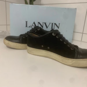 Svarta Lanvins  - Snygga svarta sneakers från Lanvin med ovandel i mocka och detaljer i skinn. Klassisk rund tå, svarta snören och vit platt sula som ger en clean look. Tillverkade i Portugal och levereras med originalkartong.                                                                  Pris kan diskuteras💸