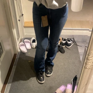 Mörkblå bootcut jeans med hög midja - Säljer ett par mörkblå jeans med bootcut och hög midja. Jeansen har klassiska fem fickor, gylf med dragkedja och knapp samt snygga kontrastsömmar. Materialet är stretchigt denim som sitter tajt upptill och släpper ut vid benslutet.