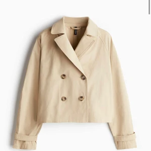 Beige kort skepparkavaj från H&M trenchcoat  - Kort skepparkavaj trenchcoat i beige bomull från H&M. Jackan har dubbelknäppning med stora knappar, klassisk krage och snygga detaljer baktill. Perfekt för dig som gillar stilren och clean look med en twist. OBS: KOMMER STRYKA DEN INNAN JAG SKICKAR IVÄG DEN! 