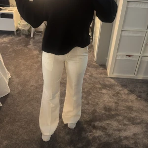 Vita bootcut byxor med fickor - Snygga vita byxor med bootcut passform och stora fickor framtill. Byxorna har medelhög midja och stängs med dragkedja och knapp. Perfekta för dig som vill ha en clean och fräsch look med lite 70-talsvibe.