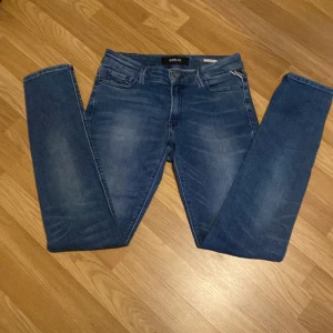 Blå Replay jeans, midwaist, storlek 29/32 - Säljer ett par klassiska blå jeans från Replay med snygg tvätt och diskreta slitningar. Modellen har fem fickor, dragkedjegylf och ikonisk bakficka med broderad detalj. Jeansen är i stretchigt denim och har en normal passform med midwaist. Kom med pris förslag