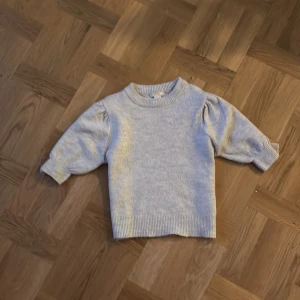 Ljusgrå stickad tröja Gina Tricot - Supermjuk off-white stickad tröja från Gina Tricot med rund halsringning och puffiga ärmar. Tröjan har ribbade muddar vid ärmslut och nederkant, perfekt för lager på lager under kyliga dagar. Lite nopprig men kan enkelt fixas med en noppermaskin.