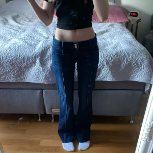 Blå bootcut jeans från Gina Tricot - Snygga blå jeans från Gina Tricot med bootcut passform och låg midja. Jeansen har framfickor, dubbla silverknappar och markerade sömmar längs benen. Säljer då dom aldrig kommit till användning.