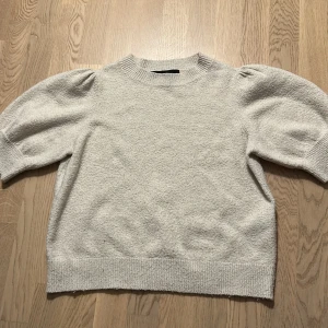 Ljusgrå stickad tröja med puffärm - Superfin ljusgrå stickad tröja med puffiga ärmar och ribbade muddar. Tröjan har en klassisk rund halsringning och är perfekt för dig som gillar en enkel men trendig look. Passar snyggt till både jeans och kjol.