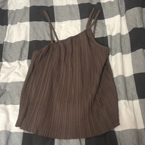 Brun ribbad linnetopp från BikBok - Säljer en brun ribbad linnetopp från BikBok i storlek S. Toppen har smala axelband och ett snyggt plisserat tyg som ger en cool struktur. Perfekt att styla med jeans eller kjol för en trendig look.