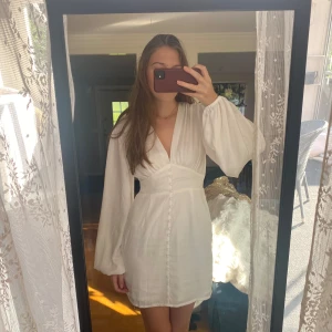 Student klänning  - Superfin vit kort klänning med v-ringning och långa puffärmar. Passar perfekt till student eller vad som. Den är använd och syns inte på långt håll men den är lite sliten 