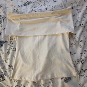 Vit axelbandslös tubtopp från H&M - Säljer en stilren vit tubtopp från H&M i storlek S. Toppen är axelbandslös med en bred kant upptill som ger en snygg offshoulder-look. Tillverkad i mjuk bomullsmix som sitter skönt och passar perfekt till sommarens outfits. Använt 1-2 gånger.