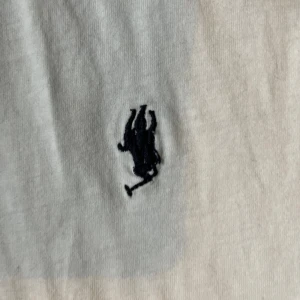 Vit t-shirt från Polo Ralph Lauren M - Vit t-shirt från Polo Ralph Lauren i 100% bomull med klassisk passform. T-shirten har korta ärmar och den ikoniska broderade polospelaren i mörkblått på bröstet. Enkel och stilren design som funkar till allt.