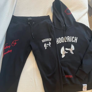 Svart hoodie och byxor från Hoodrich  - Svart hoodie och byxor från Hoodrich med stor vit logga och duvor framtill, samt broderad text och duvor i vitt och rött på ryggen. Snygga detaljer och streetkänsla. Nästan aldrig använda.