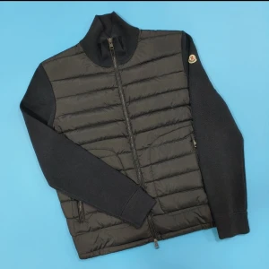 MONCLER CARDIGAN  - Snygg svart pufferjacka från Moncler med quiltad framsida och stickade ärmar. Jackan har hög krage, dragkedja framtill och två fickor med dragkedja. Klassisk Moncler-logga på ärmen och ribbade muddar för extra stilpoäng. Följer med Nfc samt tags. Pris kan diskuteras vid snabb affär 