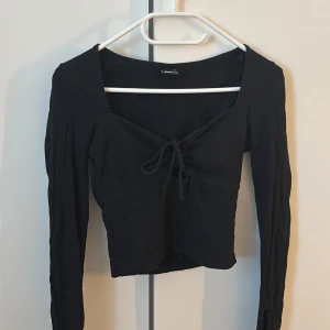 Svart långärmad topp - Svart långärmad topp från Gina Tricot i storlek XS. Passar även storlek S. Toppen har en snygg croppad passform med knytning framtill och ringning. 