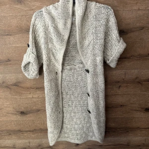 Beige stickad kofta från ONLY - Säljer en chunky stickad kofta från ONLY i beige nyans. Koftan har korta ärmar med uppvik och knappar framtill. Den är öppen framtill och har en mysig, oversized känsla. Perfekt att slänga över en t-shirt eller topp för extra värme.