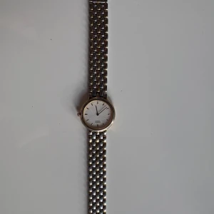 Seiko Quartz klocka i silver och guld - Klassisk Seiko Quartz klocka med rund urtavla i vitt och stilrena guldfärgade index. Armbandet är i metall med både silver- och guldfärgade länkar. Enkel och tidlös design som passar till många stilar. Urtavlan är minimalistisk utan siffror och har tre visare. Klockan har nybygg batteri. Köpt för 4500kr väldigt nyligen men säljer eftersom den aldrig kommer till användning. Glaset är lite repigt därav pris. Priset kan diskuteras via snabbaffär 