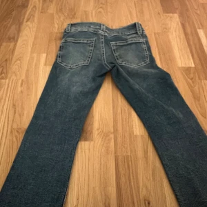 Blå bootcut jeans från Gina Tricot - Snygga blå jeans från Gina Tricot i storlek 164. Jeansen har klassisk femficksmodell, tydliga sömmar och bootcut-ben. Materialet är jeans med lätt tvättad look och dubbla silverfärgade knappar framtill.