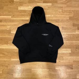 Svart Essentials Fear of God hoodie - Svart hoodie från Essentials Fear of God i storlek M. Klassisk oversized passform med huva och känguruficka. Diskret logga på bröstet och ärmen. Mjuk bomullsblandning som passar perfekt till streetwear-stilen.