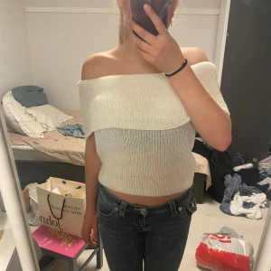 Vit offshoulder stickad topp - Säljer en vit, stickad offshoulder topp i croppad modell. Toppen är ribbad och har en bred, vikt kant över axlarna. Den är vädligt stretchig och tunn. Använt max 3 gånger så den är som ny.
