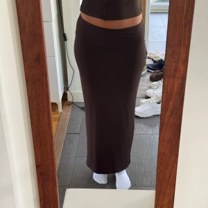 Mörkbrun långkjol i stretchigt tyg - Säljer en mörkbrun långkjol med tight passform och hög midja. Kjolen är enkel och stilren utan mönster, sydd i ett stretchigt och mjukt material som sitter snyggt mot kroppen. 