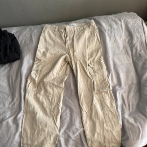 Beiga cargobyxor från Bershka - Säljer ett par beiga cargobyxor från Bershka med flera stora fickor på sidorna och bak. Byxorna har en avslappnad passform och är tillverkade i bomull. Perfekta för en chill och trendig look.