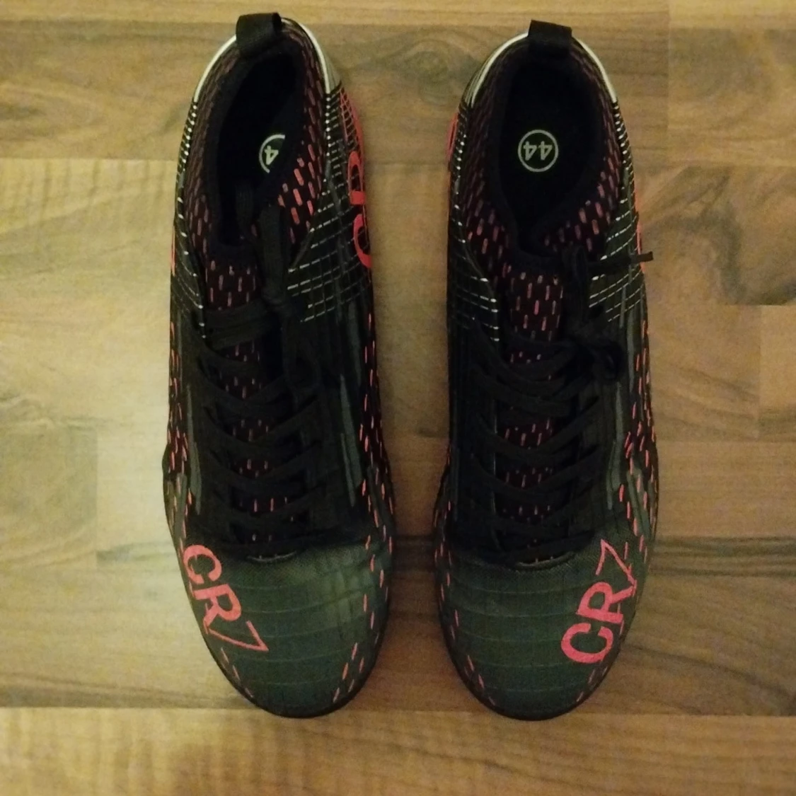 Svarta CR7 fotbollsskor med ljus röda detaljer