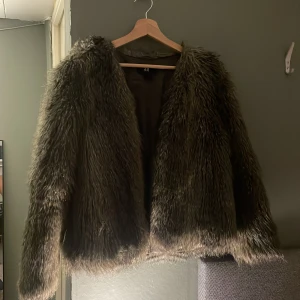 Mörkgrå/brun pälsjacka från H&M - Säljer en fluffig och snygg mörkgrå/brun pälsjacka från H&M. Jackan har lång pälsimitation, rak passform och långa ärmar. Sparsamt använd, så inga defekter