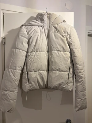Vit pufferjacka från Zara med huva - Säljer en snygg vit pufferjacka från Zara i storlek S. Jackan har en stor, mysig huva och dragkedja framtill. Den är quiltad och har en loose passform som ger en chill vibe. Perfekt för kalla dagar och enkel att styla med dina favoritjeans.