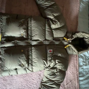 Grön dunjacka från Fjällräven XXXS - Säljer en grön dunjacka från Fjällräven i storlek XXXS. Jackan har huva med gula snören, stora fickor med knappar och klassisk Fjällräven-logga på bröstet. Perfekt för kalla dagar med sin puffiga och quiltade design. Den är köpt förr förra vintern i väldigt fint skick lite små skavanker så som att de vita sakerna på snörena är lite slitna men de e inget som syns. Väldigt skön och fin🥰 dom är stora i storleken jag har vanligtvis S men denna passar perfekt också med en lite tjockare tröja under