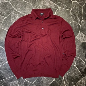 Uniqlo piketröja - Snygg vinröd pikétröja från Uniqlo i stickad bomull. Tröjan har klassisk krage, två knappar framtill och långa ärmar. Perfekt för dig som vill ha en chill men stilren look. Passar dig som gillar enkel design och mjuka material.