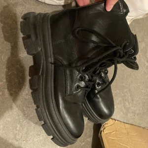 Svarta chunky boots i skinn - Säljer ett par svarta boots med chunky sula och snörning. Skorna är i skinn och har en robust, cool look med rund tå och grov yttersula. Perfekta för dig som vill ha en edgy stil och gillar boots med attityd.