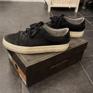 Svarta Sneaky Steve sneakers mocka - Svarta sneakers från Sneaky Steve i mocka med rund tå och platt vit sula. Skorna har snörning och detaljer i svart skinn på hälen. Stilren och klassisk modell som passar till allt. Storlek 41.