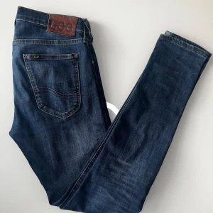 Lee Jeans Luke - Snygga mörkblå jeans från Lee med klassisk femficksdesign och brunt läderpatch med logga bak. Jeansen har raka ben och kontrastsömmar, vilket ger en tidlös look. Perfekta för dig som gillar stilrena och bekväma jeans. W29 L32