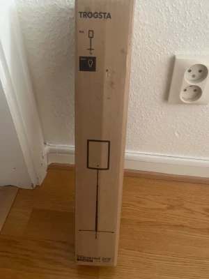 TROGSTA golvlampa - TROGSTA golvlampa från IKEA, ny i oöppnad originalförpackning. Modern och stilren design, perfekt för vardagsrum eller sovrum. Glödlampa ingår ej. Kartongen är i gott skick med mindre märken från förvaring. Ny oanvänd 