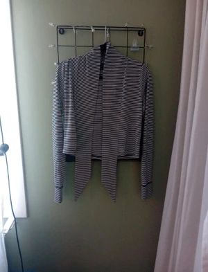 Randig croppad bolerotopp - Säljer en svartvit randig bolerotopp med långa ärmar och croppad passform. Toppen har långa knytband framtill som ger en snygg omlott-look. Perfekt att slänga över ett linne eller klänning för en cool layering-effekt.