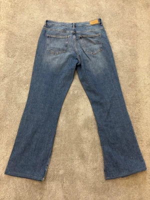 Blå bootcut jeans med slits från Vero Moda - Snygga blå jeans från Vero Moda med bootcut passform och slitsar längst ner på benen. Klassisk femficksmodell med normal midja och dragkedja fram. Jeansen har en lätt tvättad look och är gjorda i mjukt denimtyg som sitter skönt.