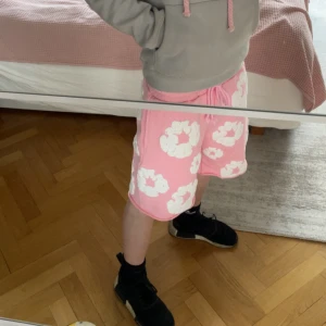 Rosa shorts från denim tears - Säljer ett par rosa shorts från denim tears med vita blommiga mönster. De har elastisk midja med snörning och är tillverkade i ett mjukt material som känns skönt mot huden. 9/10 skick. Använda 3 gånger, alla tags och mer följer med. Skriv för mer information/ bilder. MVH John 