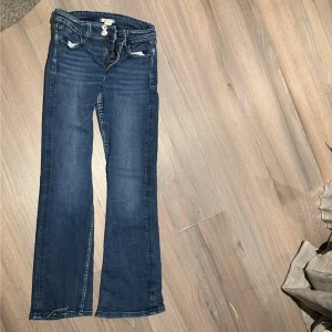 Blå bootcut jeans från Gina Tricot - Snygga blå jeans från Gina Tricot i storlek 158. Modellen har bootcut-ben, klassiska fem fickor och coola detaljer på bakfickorna. Jeansen har knappstängning och är tillverkade i mjukt denimtyg som sitter skönt hela dagen. väldigt bra skick använda några gåner 