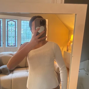 Vit ribbad oneshoulder topp - Säljer en vit ribbad topp med oneshoulder-design och lång ärm. Sitter tight och har en snygg asymmetrisk skärning som ger en modern vibe. Perfekt för dig som vill sticka ut lite extra med din stil.
