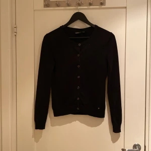 Svart kofta från KappAhl XS - Svart, klassisk kofta från KappAhl i storlek XS. Den har rund halsringning, långa ärmar och knappar hela vägen framtill. Perfekt att slänga över en t-shirt eller linne för en chill look. Materialet känns mjukt och skönt mot huden.