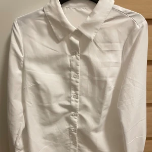 Vit klassisk skjorta med knappar - Snygg vit skjorta med klassisk krage och knappar hela vägen framtill. Skjortan har lång ärm och är gjord i ett mjukt bomullstyg som känns skönt mot huden. Perfekt för dig som gillar stilrena och enkla plagg med clean look.