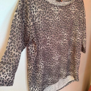Leopardmönstrad topp  - Snygg topp från ONLY i storlek S med leopardmönster i beige och grå toner. Modellen har rund hals, trekvartsärm och är kortare framtill. Materialet är mjukt och lätt, vilket gör den skön att bära och aningen transparent. Stor i storleken.