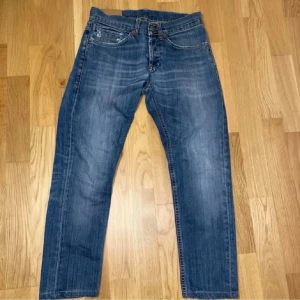 Blå Dondup jeans 29/30 - Säljer ett par klassiska blå jeans från Dondup med raka ben och snygga slitningar. Jeansen har fem fickor, dragkedja och knappstängning samt detaljerade bakfickor med broderad söm. Perfekt för dig som gillar en tidlös och avslappnad stil.