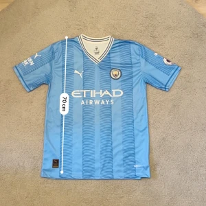 Manchester City Haaland #9 matchtröja - Manchester Citys officiella matchtröja från Puma med Haaland och nummer 9 på ryggen. Tröjan är ljusblå med tunna mörkblå ränder, har korta ärmar och V-ringad krage med vita detaljer. Materialet är lätt och andas, perfekt för fotboll. Premier League-märke på ärmen.Aktiv 24/7✅ Skickas inom 24h📦🚚 Kan gå ner i hugget 😃✅ Hör av er via frågor⁉️