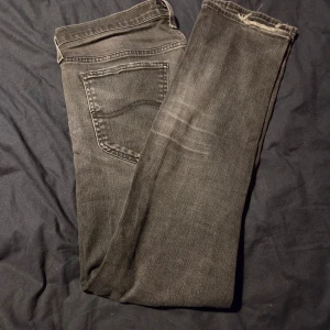 Svarta slim fitt jeans från Lee - Säljer ett par svarta jeans från Lee med klassisk femficksdesign och raka ben. Jeansen har en snygg tvättad look. Passar dig som gillar en enkel och stilren vibe.
