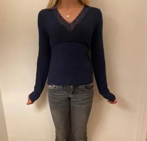 Mörkblå långärmad topp med spets Gina Tricot - Mörkblå långärmad topp från Gina Tricot med snygg v-ringning och spetsdetalj längs halsen. Toppen har en slim passform och är perfekt att styla med jeans eller kjol. Materialet känns mjukt och följsamt mot huden.