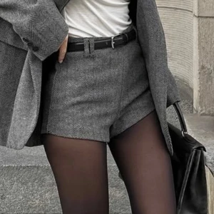 Grå mönstrade mini shorts från Gina Tricot - Snygga grå mini shorts från Gina Tricot med klassiskt fiskbensmönster. Modellen är högmidjad och har en stilren, skräddad look som passar till kavaj eller tights. Materialet är mjukt och känns lyxigt, perfekt för dig som gillar trendiga och dressade outfits. Aldrig använda