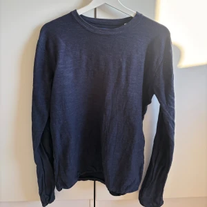 Mörkblå långärmad tröja Jack & Jones - Snygg mörkblå långärmad tröja från Jack & Jones Originals. Enkel och stilren design med rund hals och mjukt material som känns skönt mot huden. Perfekt att slänga på sig när det är lite kyligt ute.